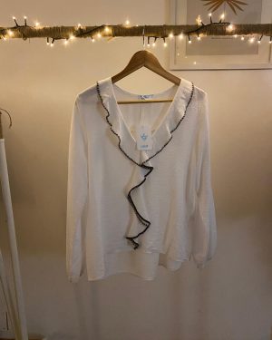 Blusa blanca fluida con detalle de volantes en el frente y ribete negro.